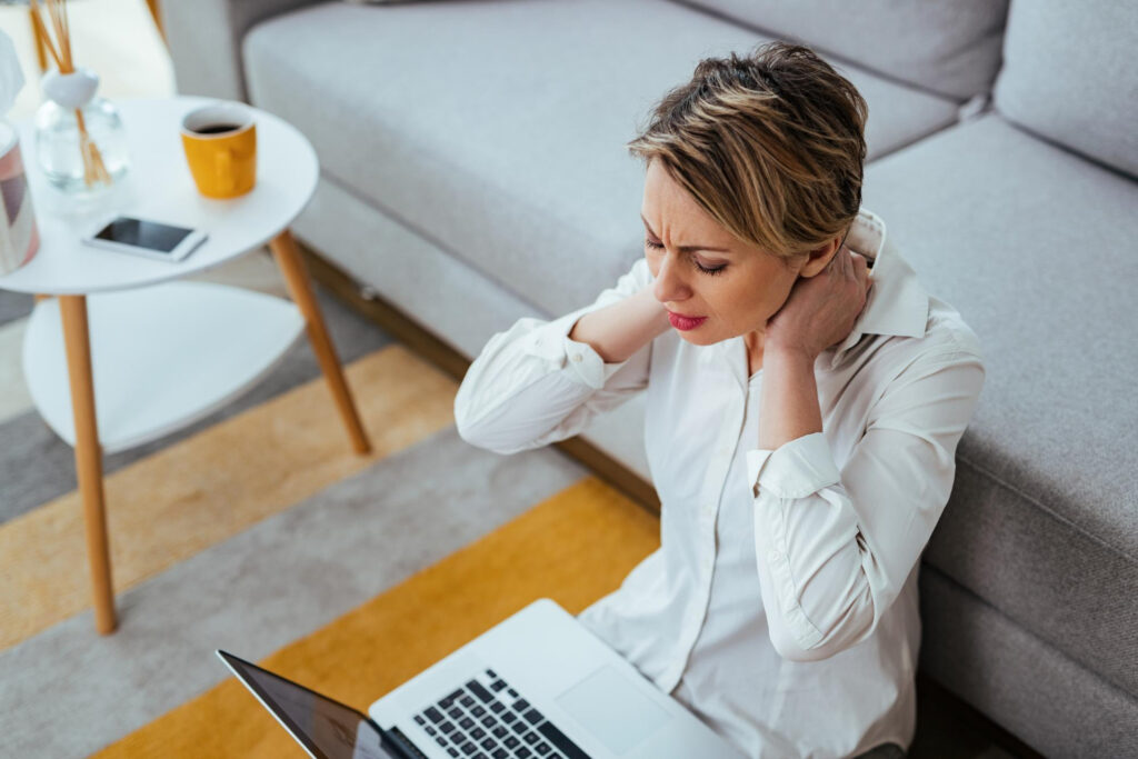 Woman sitting on the floor holding her neck that is painful.