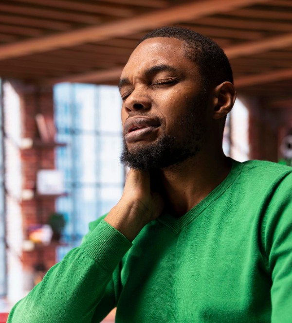 A man in a green shirt with his eyes closed in pain as he holds the muscle tension in his neck.